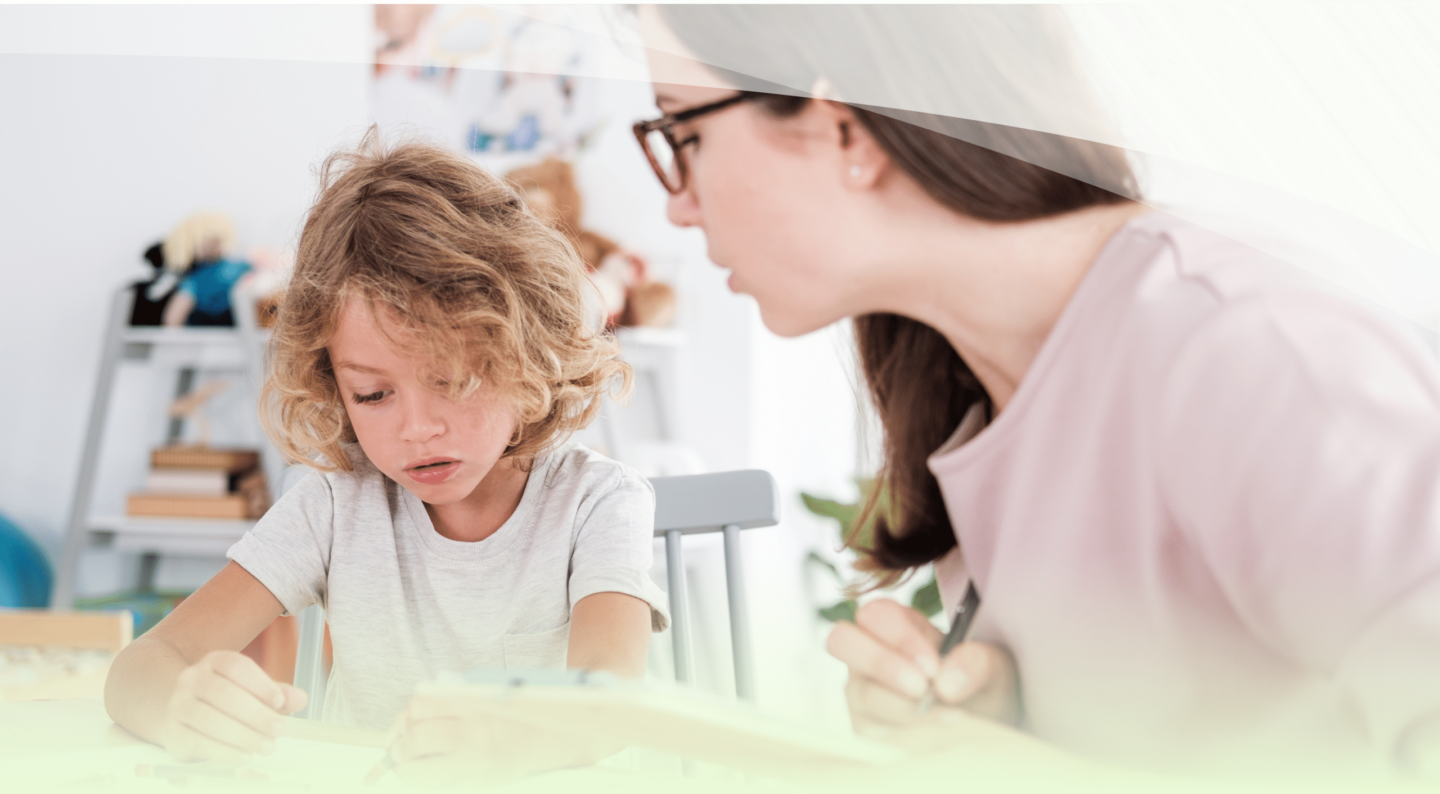 Teacher closely supporting a young student as they work on an assignment together in a classroom.
