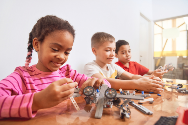 Three kids assembling a robotics kit with components at a classroom table.