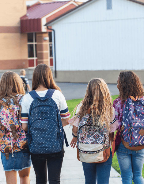 Four students with backpacks walking together toward a school building.